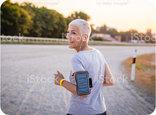 A person smiling and looking back while running on a track outside. They have short hair and medium skin tone and are wearing earpods and listening to music.
